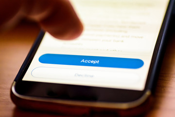 Accept button on smartphone screen closeup with human finger pointing to it