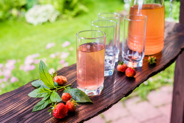One full and three empty glasses and jug of fruit juice. Strawberries and mint. Summertime.