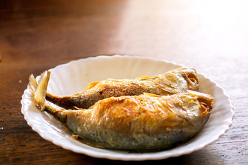 Fried mackerels on white ceramic plate and wooden table with natural sun light background. Fried mackerels popular to eat in Thailand and eat with Thai shrimp paste chili sauce (Nam Phrik Kapi).