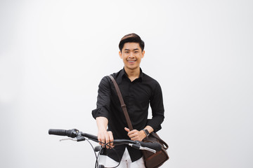 Fototapeta na wymiar Young handsome asian man against the backdrop of white wall sits on a bicycle