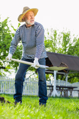 Grey-haired man in straw hat using shovel while digging ground © zinkevych
