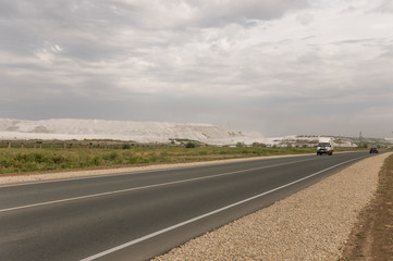 Big autumn field with trees far away and clouds in the blue sky. Asphalt road. Travelling