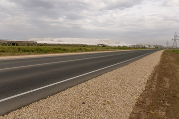Big autumn field with trees far away and clouds in the blue sky. Asphalt road. Travelling