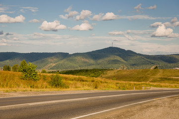 Big autumn field with trees far away and clouds in the blue sky. Asphalt road. Travelling