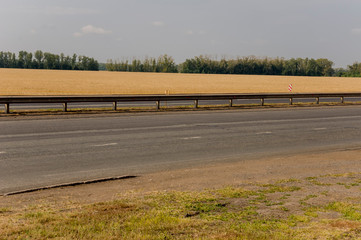 Big autumn field with trees far away and clouds in the blue sky. Asphalt road. Travelling