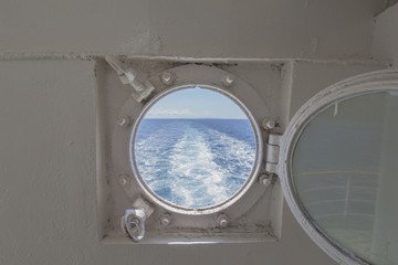metal porthole scuttle on a fast ferry with the view of the backwash and waterway