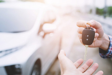Car key, businessman handing over gives the car key to the other woman on car background.