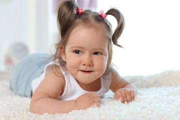 Adorable little baby girl lying on bed in room