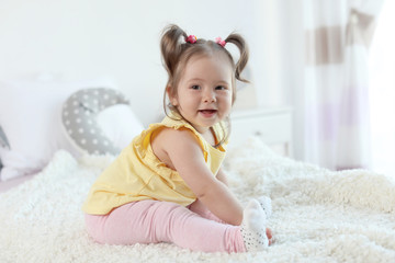 Adorable little baby girl sitting on bed in room