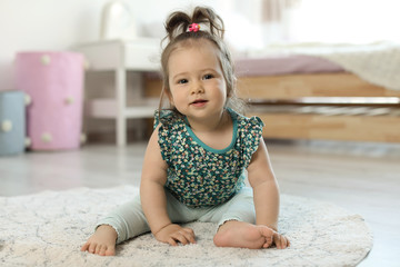 Adorable little baby girl sitting on floor in room