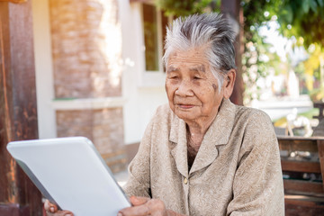 Happy Asian old woman / grandmother smiling and using tablet pointing finger on touching screen for typing chating sms message to Grandchildren