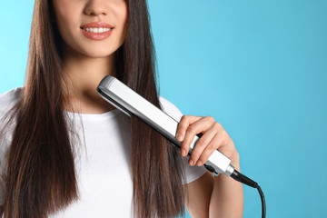 Happy woman using hair iron on color background, closeup