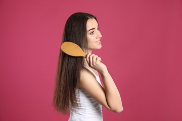 Beautiful smiling young woman with hair brush on color background