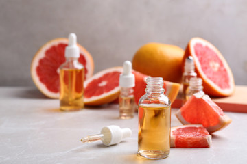 Bottles of essential oil and grapefruits on grey table, space for text
