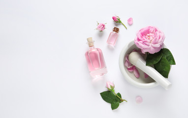 Composition with rose essential oil and flowers on white background, top view