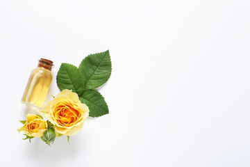 Bottle of rose essential oil and flowers on white background, top view