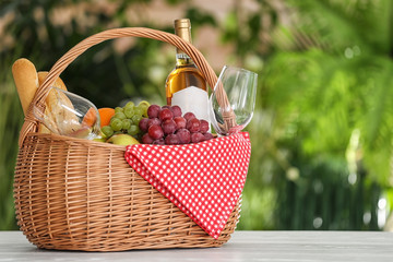 Picnic basket with products and wine on table against blurred background, space for text