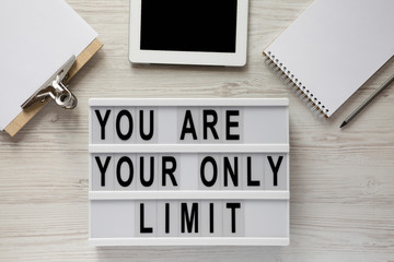 'You are your only limit' words on a modern board, clipboard with blank sheet of paper, tablet, notepad over white wooden background, top view.