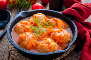 Meatballs with rice in a cast iron skillet tomato sauce on a wooden table, horizontal