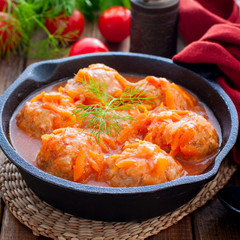 Meatballs with rice in tomato sauce and vegetables in a black cast iron pan, selective focus