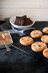 Cookies with chocolate chips and hazelnuts, on metal grill, made with oatmeal and wheat flour. Accompanied with chocolate powder and chocolate with almonds.