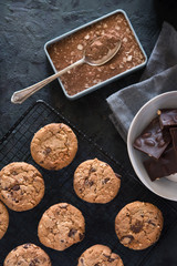 Cookies with chocolate chips and hazelnuts, on metal grill, made with oatmeal and wheat flour. Accompanied with chocolate powder and chocolate with almonds.