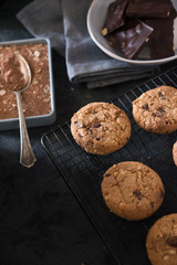 Cookies with chocolate chips and hazelnuts, on metal grill, made with oatmeal and wheat flour. Accompanied with chocolate powder and chocolate with almonds.