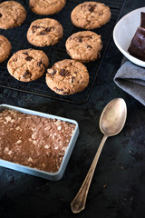 Cookies with chocolate chips and hazelnuts, on metal grill, made with oatmeal and wheat flour. Accompanied with chocolate powder and chocolate with almonds.