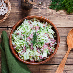 Obraz na płótnie Canvas Salad with fresh cabbage and smoked sausage on a wooden table, top view, selective focus