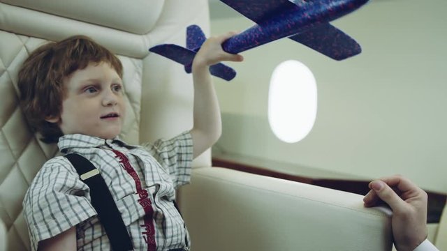Pilot carries boy playing with blue plane toy, imagination dreaming of being a pilot future, on a boarder of private jet plane. RED HELIUM.