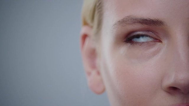 Close-up Macro View Of Beauty Female Face Part With Blue Eye Rolling Up. Pretty Portrait Of Lovely Blonde Girl Playing With Eyes Isolated On Gray Background.