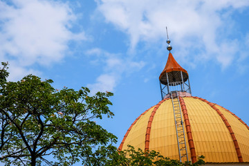 Orange castle's dome with trees and blue sky.Orange dome with a bell on top surrounded by blue sky and trees.