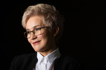 stylish elderly woman in glasses and black jacket on a black background	