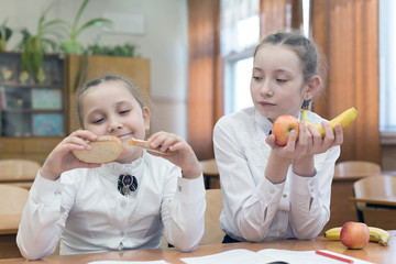 A vegetarian girl looks at her friend's food with envy. Schoolgirl with fruit in her hands envies...