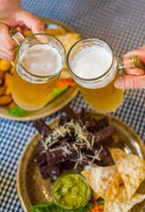 Close-up view of a two glass of beer in hand. Beer glasses clinking in bar or pub on table with food background