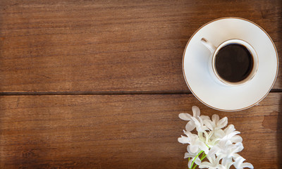 Black Coffee Cup on wooden table top view with white flowers