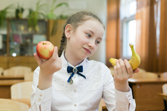 Girl in school uniform chooses food for lunch. School girl on a diet makes a choice between fruit and a harmful sandwich.