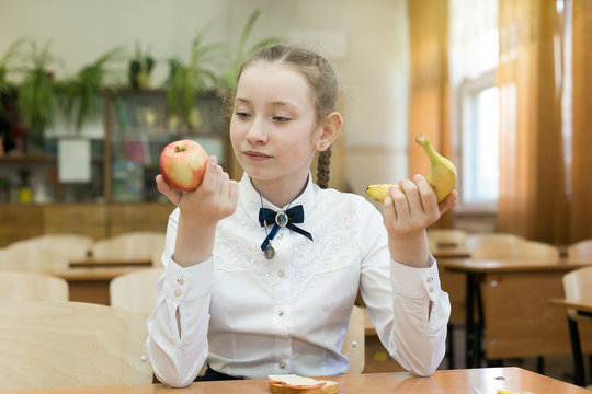 School girl on a diet makes a choice between fruit and a harmful sandwich. Girl in school uniform chooses food for lunch.