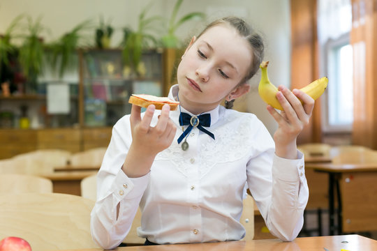 Girl in school uniform chooses food for lunch. School girl on a diet makes a choice between fruit and a harmful sandwich.