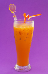 Orange milk tea in glass with spoon and drink straw on purple background