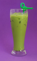 Green milk tea in glass with drink straw on purple backgroun