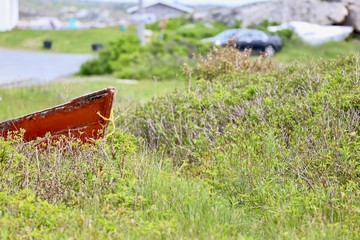 Old red boat in field of grass, abandoned, damaged