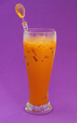 Iced orange milk tea in glass with spoon on purple background