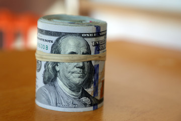 financial image of close up rolled and rubber banded American one hundred dollar bills pile on desk