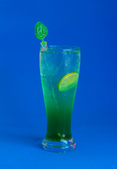 Glass of peppermint syrup and soda on blue background