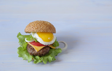 Hamburger isolated with fried egg on a wooden white background with copy space for text.