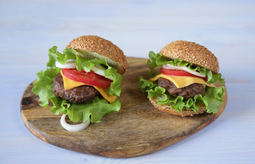 Close-up. Two perfect hamburger with beef patty, cheese, pickles, tomatoes, onions, lettuce on a wooden light blue background with copy space for text.