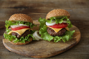 Close-up. Two hamburger with beef cutlet, with cheese, pickles, tomatoes, onions, lettuce on a wooden rustic background.