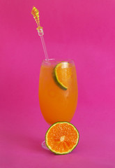 Glass of iced orange juice on pink background