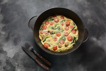 Frittata made of eggs, mushrooms, cherry tomatoes and spinach served in a pan. Italian cuisine